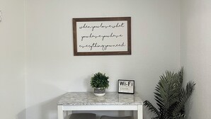 A small room with a ceiling fan, a framed inspirational quote, a small table with two chairs, a potted plant, and a Wi-Fi sign. - Escape By The Bay (Tampa)