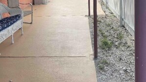 A covered patio area with a concrete floor, a white chair, a small table, and a red awning. - Escape By The Bay (Tampa)