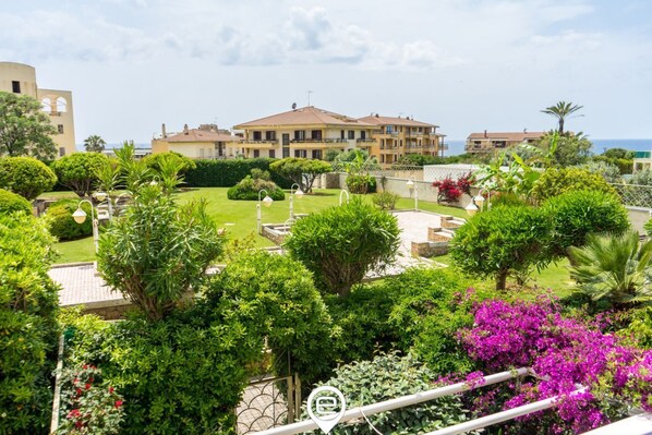 A residential area with a large building, well-maintained gardens, and a clear view of the sea.