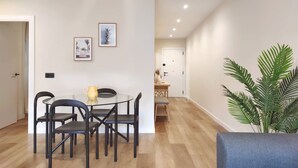 Un coin repas avec une table ronde, des chaises noires et un pichet jaune. Deux tableaux encadrés ornent le mur.