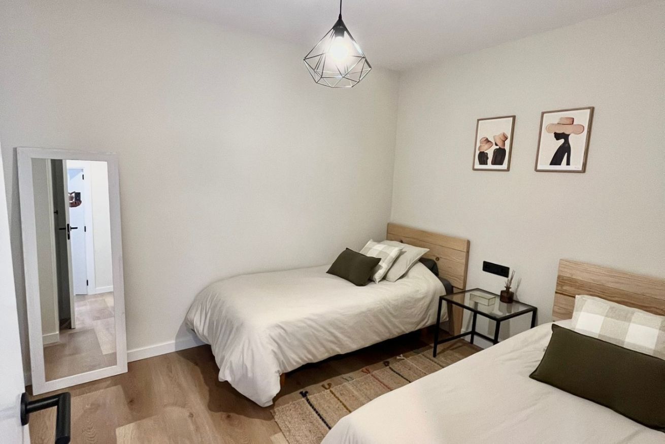 A bedroom with two beds, a bedside table, a mirror, and a hanging light fixture.