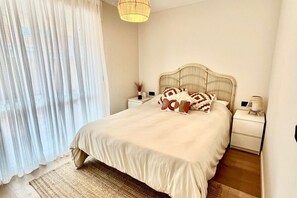 Un dormitorio con cama, mesitas de noche, lámpara y ventana con cortinas.