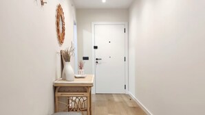 Un couloir avec une porte, une petite table ornée d’un vase et d’objets décoratifs, et un banc.