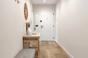 A hallway with a door, a small table with a vase and decorative items, and a bench.