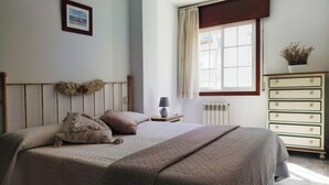 Een slaapkamer met een bed, nachtkastje, dressoir, raam met gordijnen en een radiator.