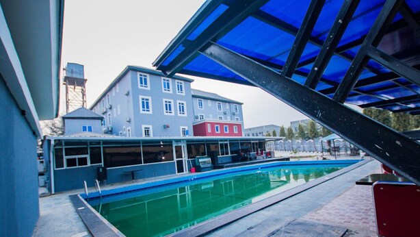 Una piscina con una struttura a tetto blu, un edificio rosso sullo sfondo e un vialetto in mattoni.