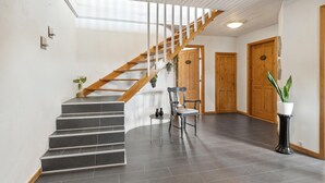 A staircase with wooden railings and dark grey steps, leading to a room with a chair and a small table.