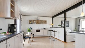 A modern kitchen with wooden cabinets, a coffee machine, and a dining area with two chairs and a small table.