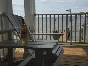 A wooden deck with a table and two chairs, overlooking a body of water with a railing.