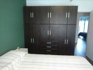 A bedroom with a large dark wooden wardrobe, a bed with a striped white duvet, and a view of a room with a bed through a doorway. - Casa Colinas 2 (Mar del Plata)