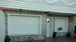 A house with stone exterior walls, large white garage doors, and a small garden area with potted plants. - Casa Colinas 2 (Mar del Plata)