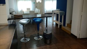 A modern kitchen with a dining area, featuring a black countertop, two bar stools, a small table with a bowl, and a fan. - Casa Colinas 2 (Mar del Plata)