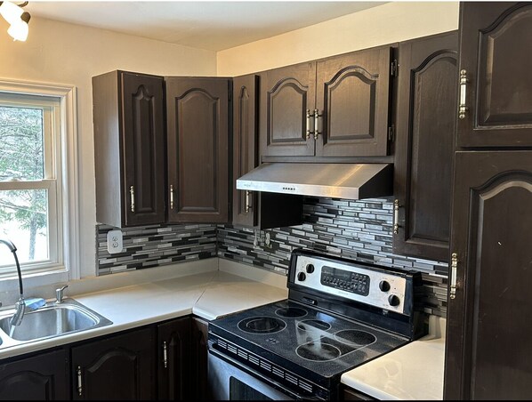 A kitchen with dark wooden cabinets, a stainless steel range hood, and a black stove.