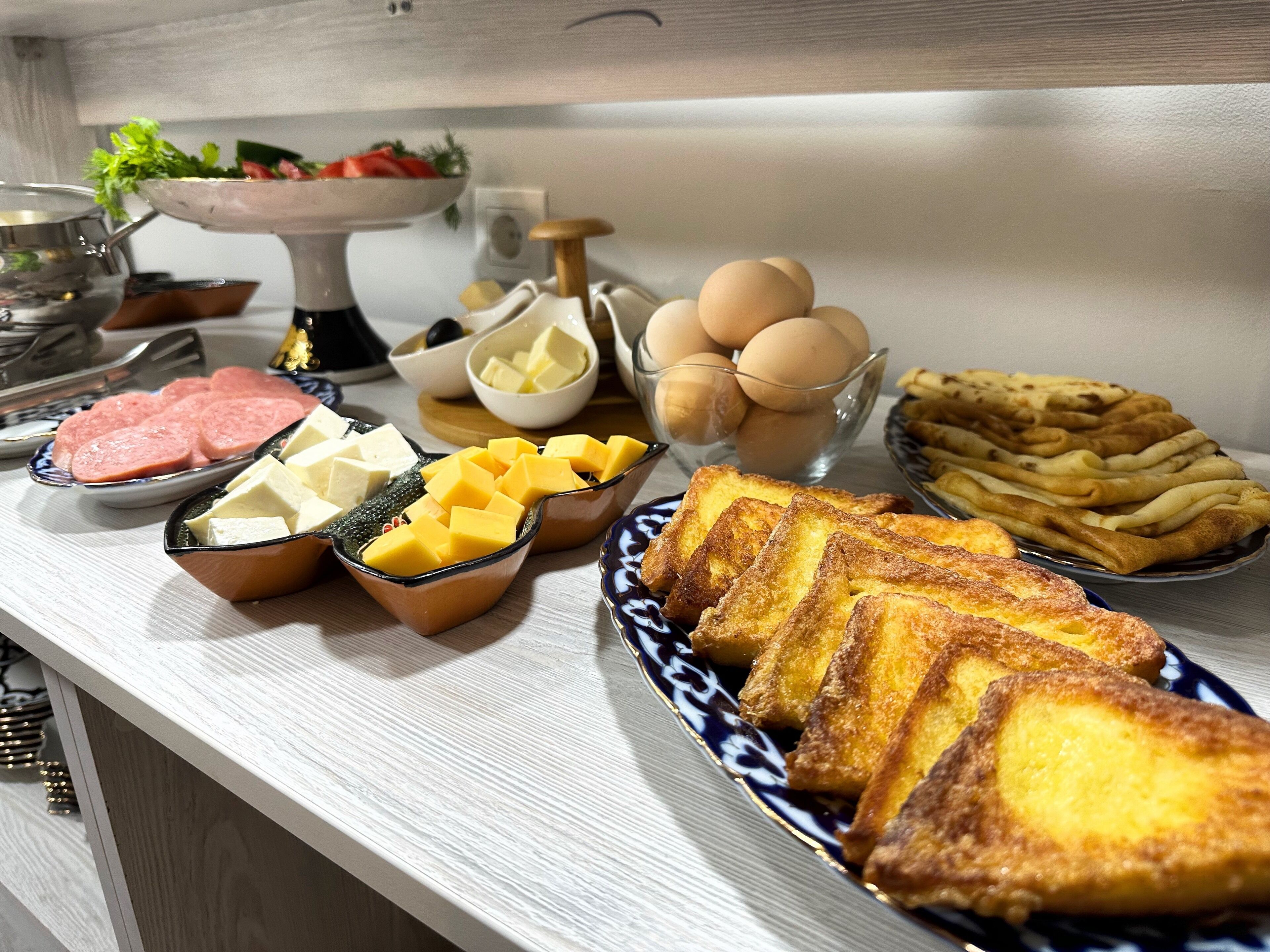 A breakfast buffet with various food items including eggs, cheese, ham, and French toast.