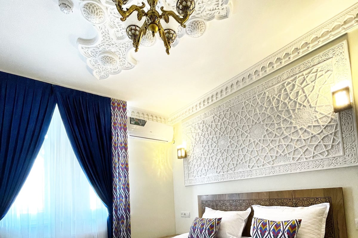 A hotel room with a large bed, a chandelier, patterned curtains, and a decorative wall.