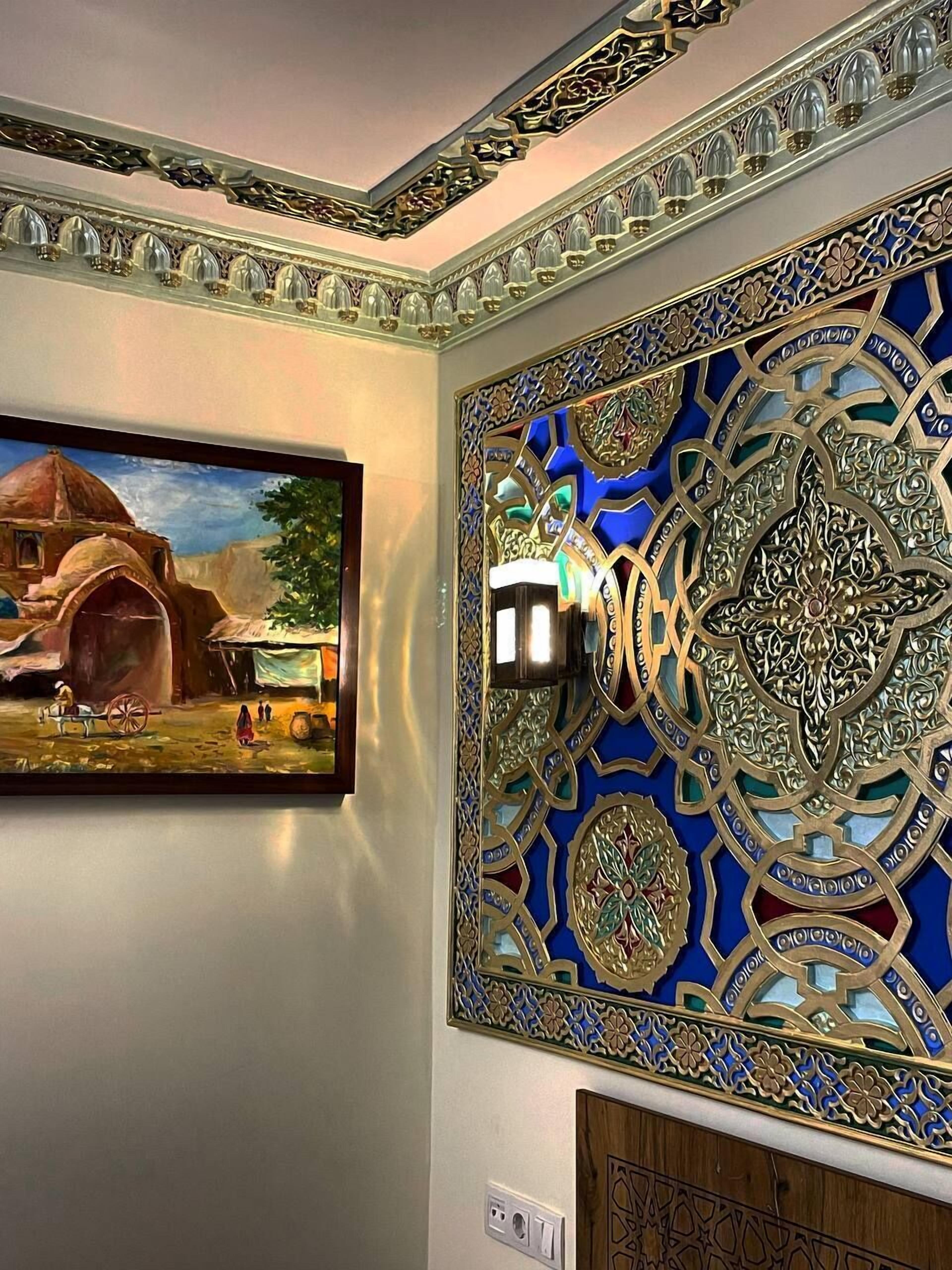 Ein Zimmer mit traditioneller Wandgestaltung in Blau und Gold, einem gerahmten Gemälde einer ländlichen Szene und einer modernen Leuchte.