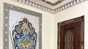 Une pièce dotée d’un grand miroir richement décoré de motifs complexes, d’une porte en bois ornée de motifs géométriques et d’un plancher en bois.