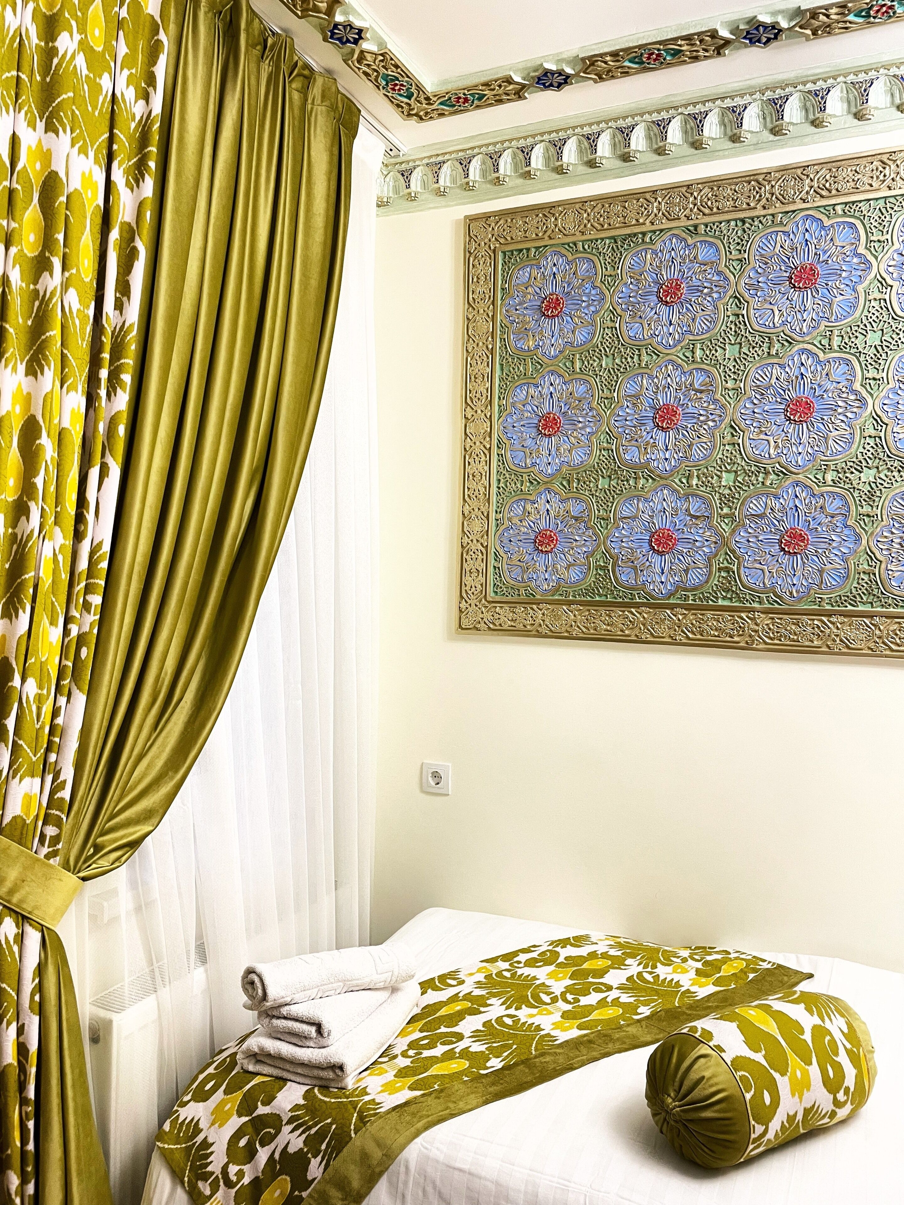 Una stanza con un letto, una coperta verde a motivi, una tenda verde e bianca a motivi e un muro decorato con una tappezzeria floreale.