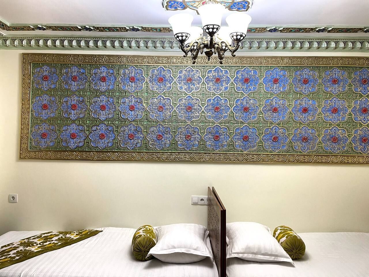 Ein Hotelzimmer mit einem großen floralen Wandteppich, einem Bett mit weißen Leinen und einer Kristallleuchtreibe.
