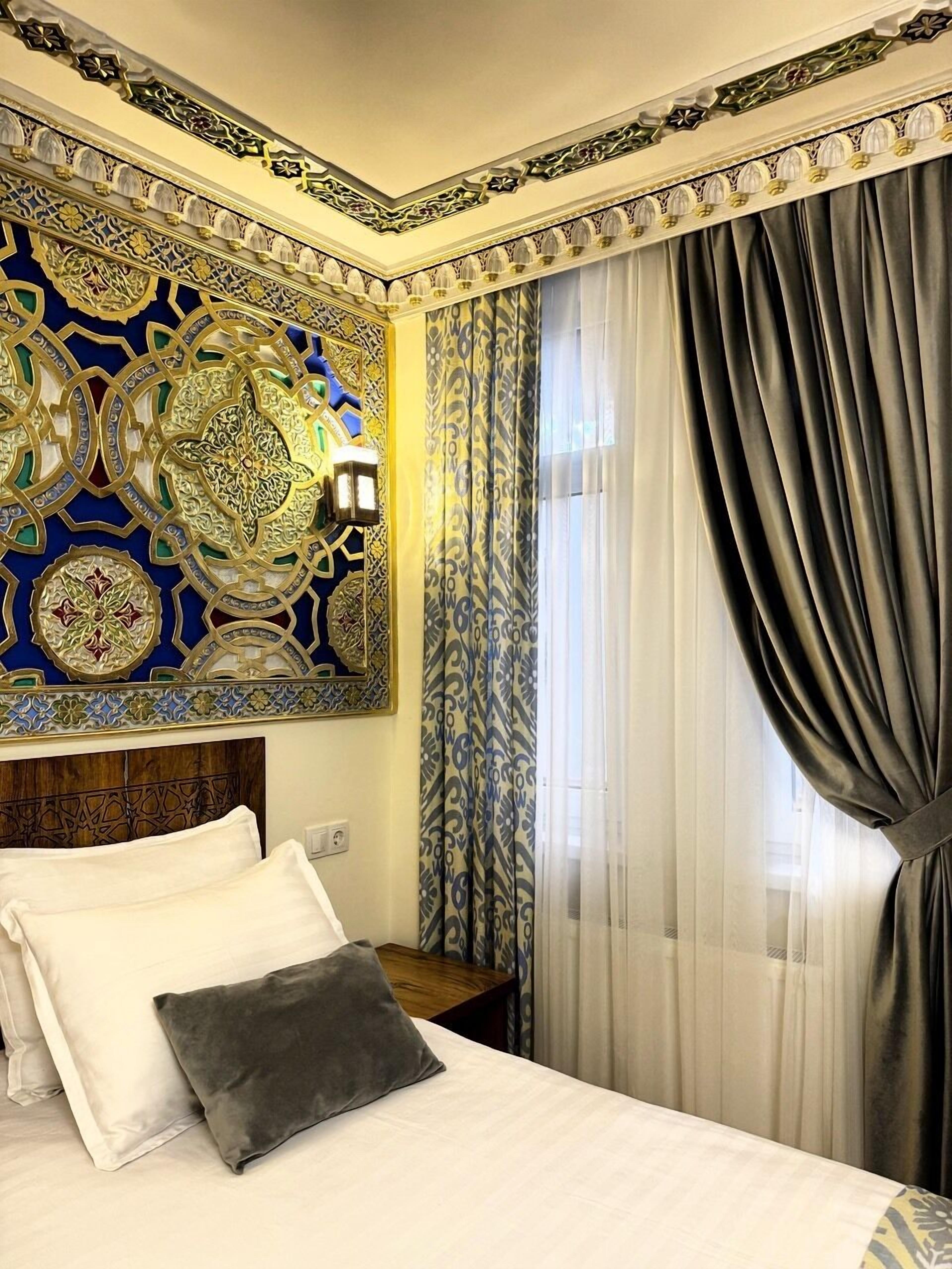 Ein Hotelzimmer mit Bett, einer Zierwand, einem Nachttisch und einem Fenster mit Vorhängen.