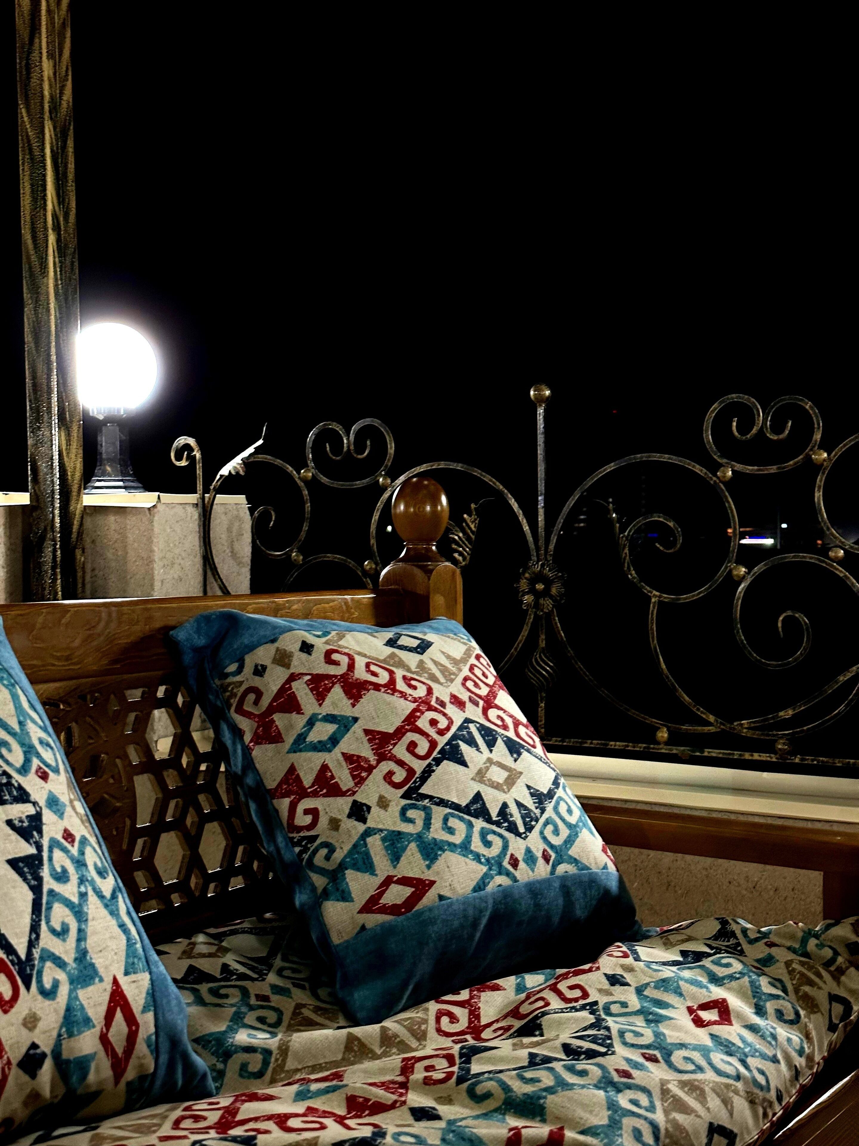 A bed with patterned pillows and a metal headboard against a dark background.