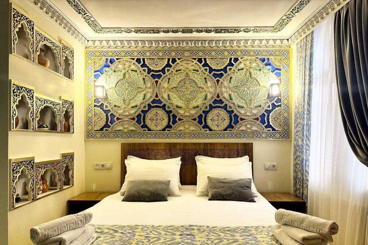 A hotel room with a large bed, ornate wall decorations, and a patterned bedspread.