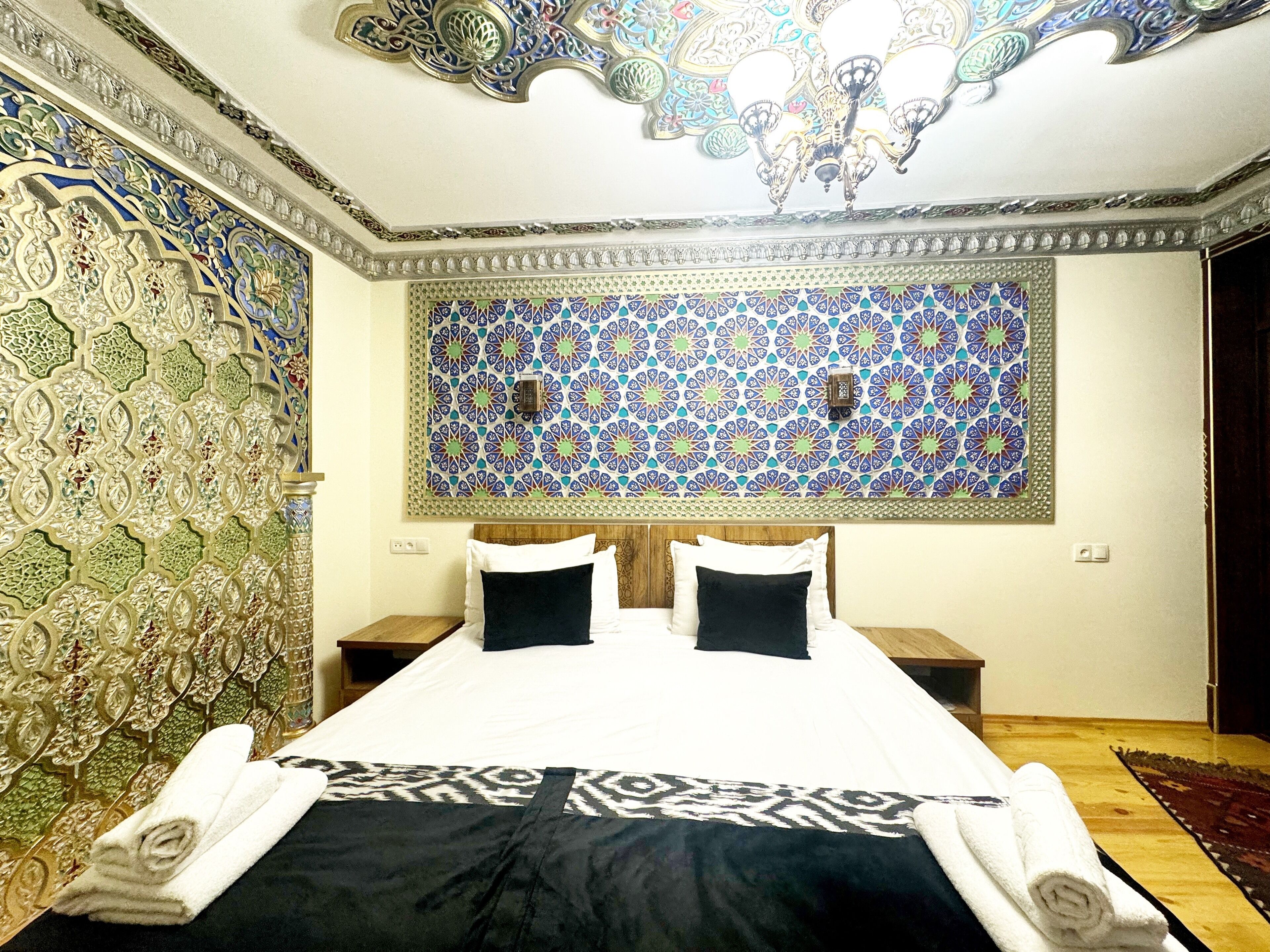 A hotel room with a large bed, two nightstands, a decorative ceiling, and a patterned wall.