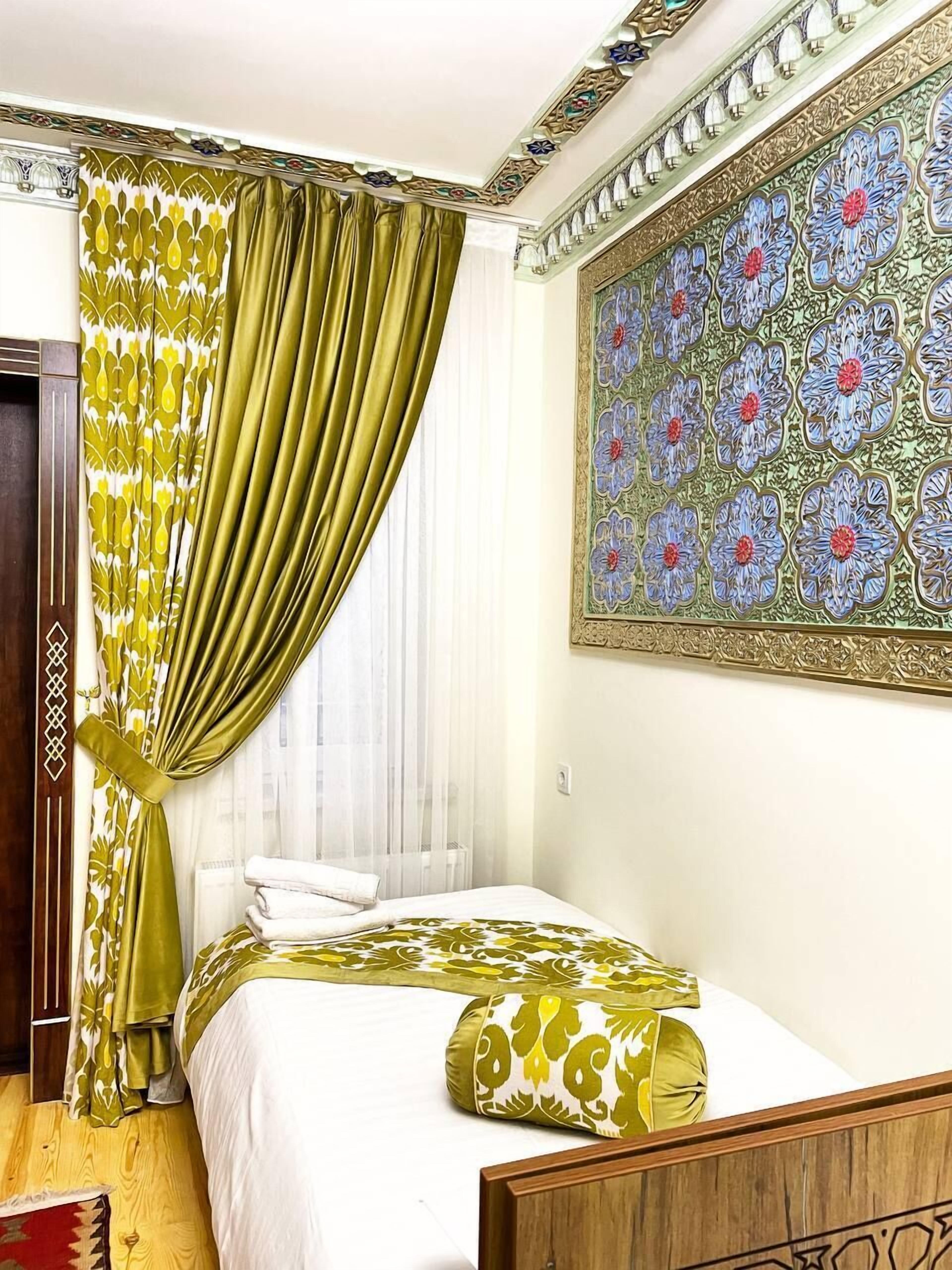 A hotel room with a bed, green curtains, a wall tapestry, and a wooden headboard.