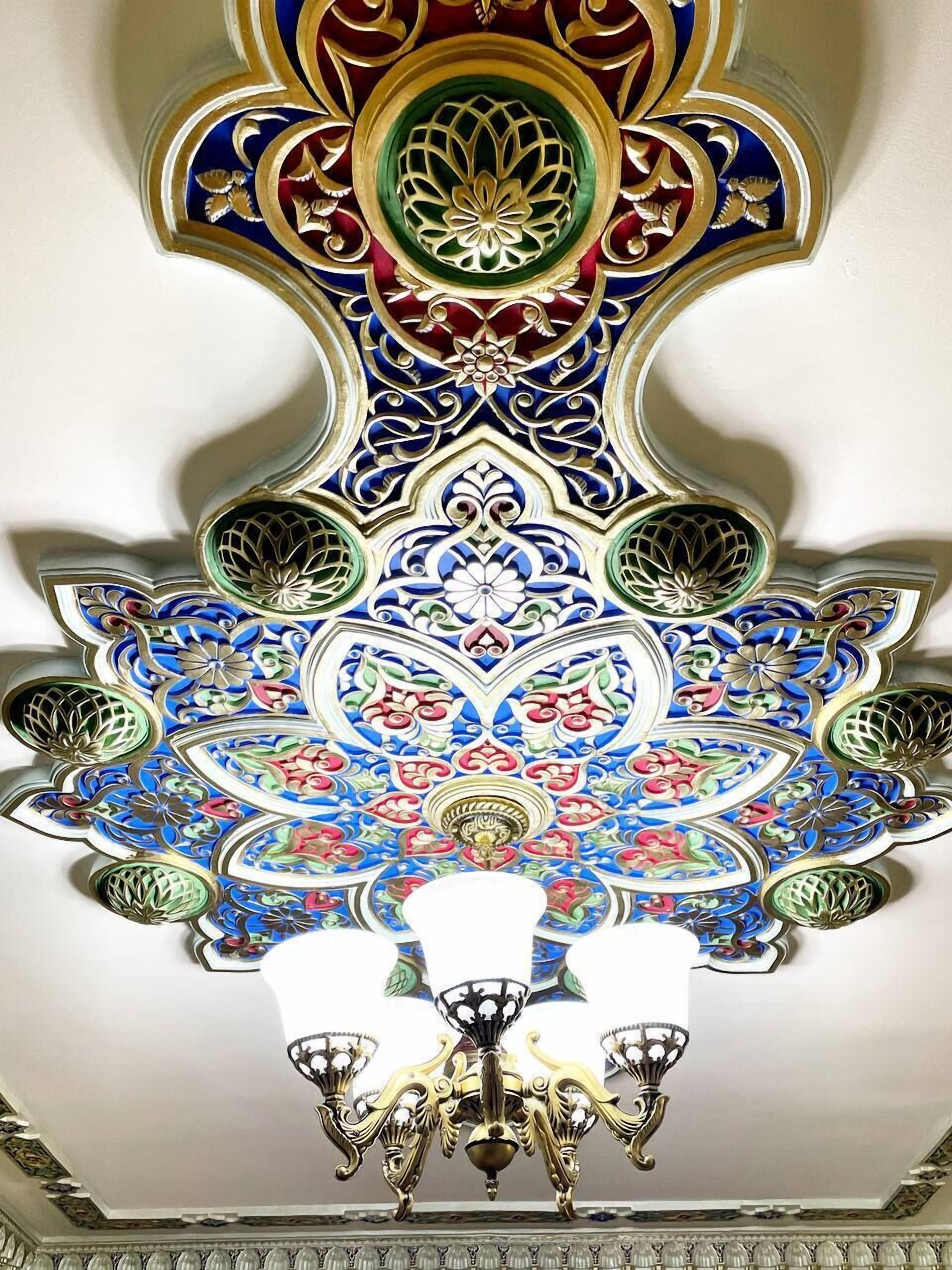 A ceiling with intricate floral and geometric patterns, a chandelier, and a domed ceiling design.