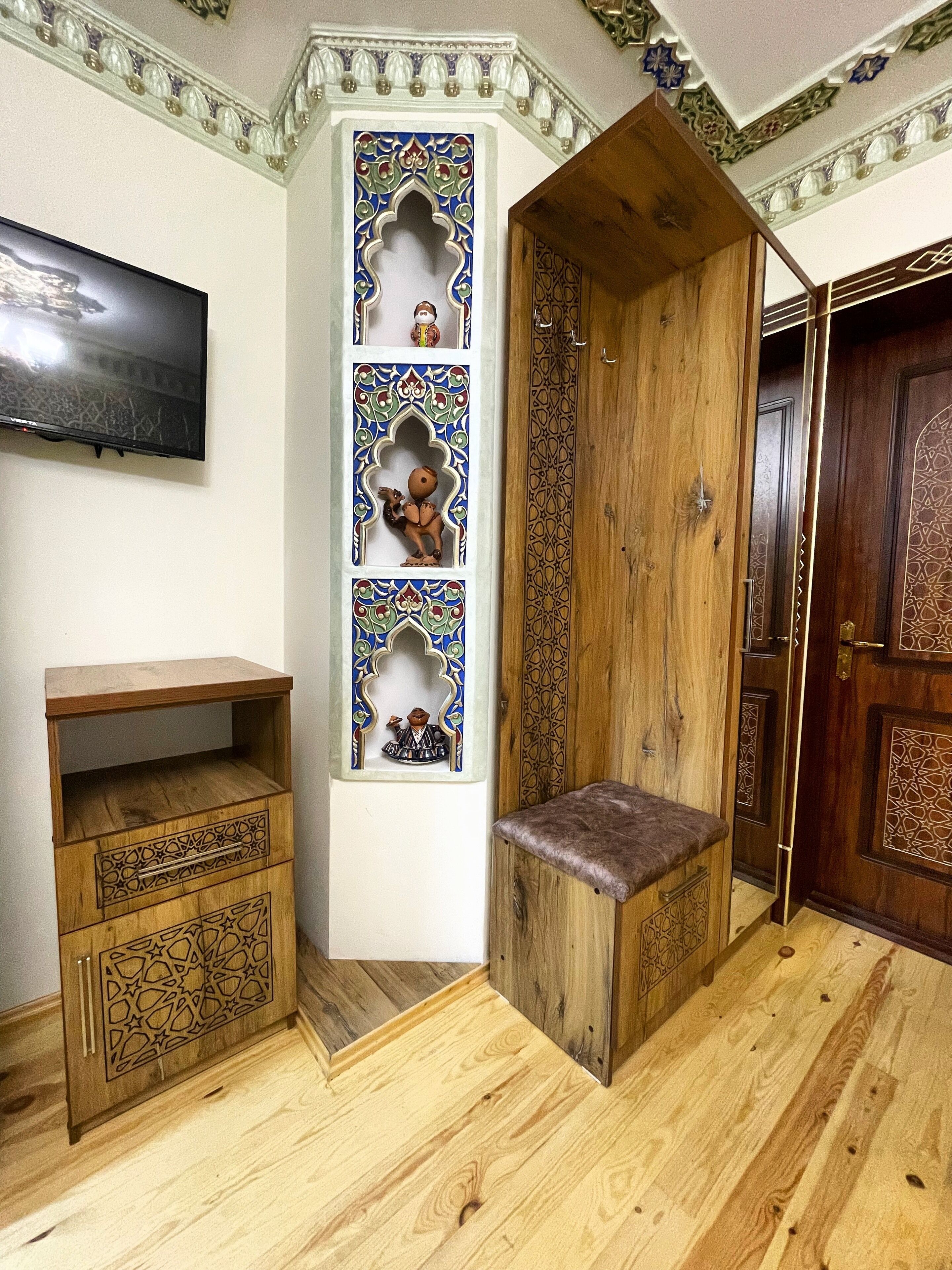 A room with a wooden cabinet, a bench, and a wall-mounted TV.