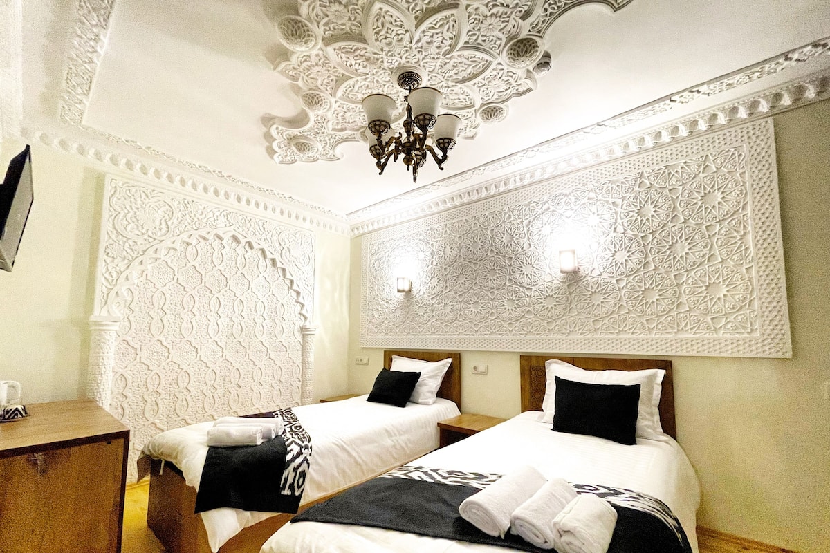 A hotel room with two beds, a wooden nightstand, and a decorative ceiling.