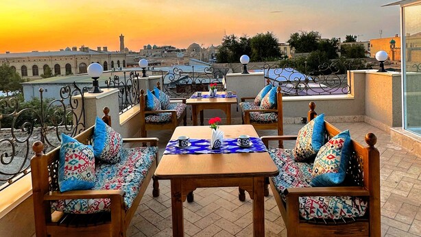 Une terrasse dotée de mobilier en bois et d’une table, offrant une vue sur le paysage urbain au coucher du soleil.