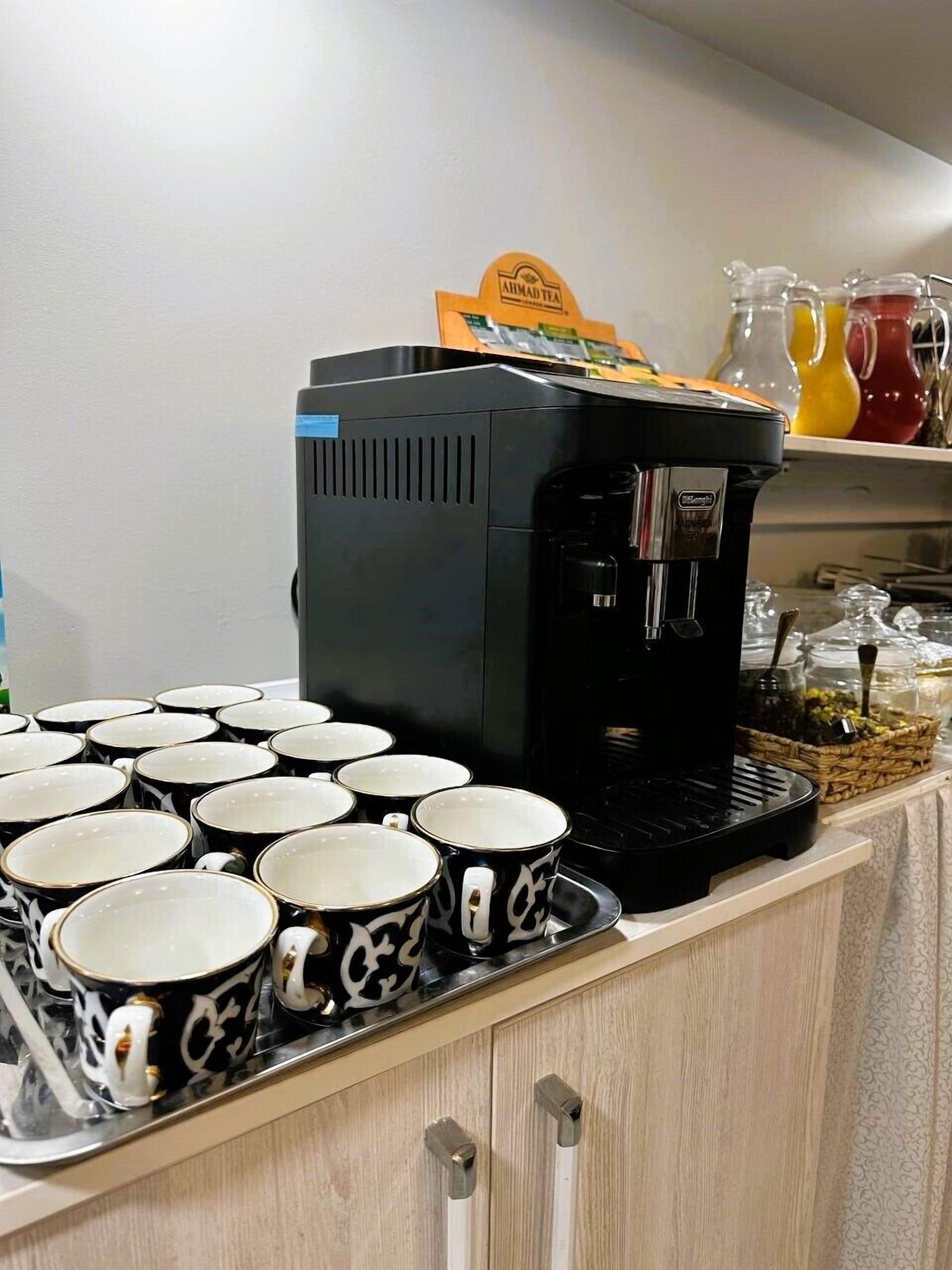 Una estación de café con una cafetera Keurig, una bandeja de tazas con estampado blanco y negro y un letrero de Té Ahmadi.