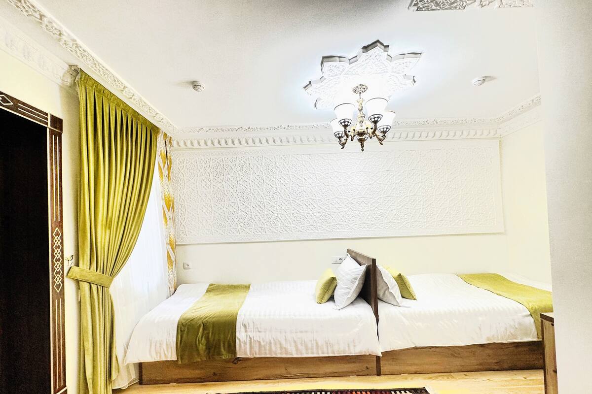 A room with a bed, a chandelier, a patterned wall, and a green curtain.
