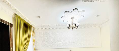 A room with a bed, a chandelier, a patterned wall, and a green curtain.