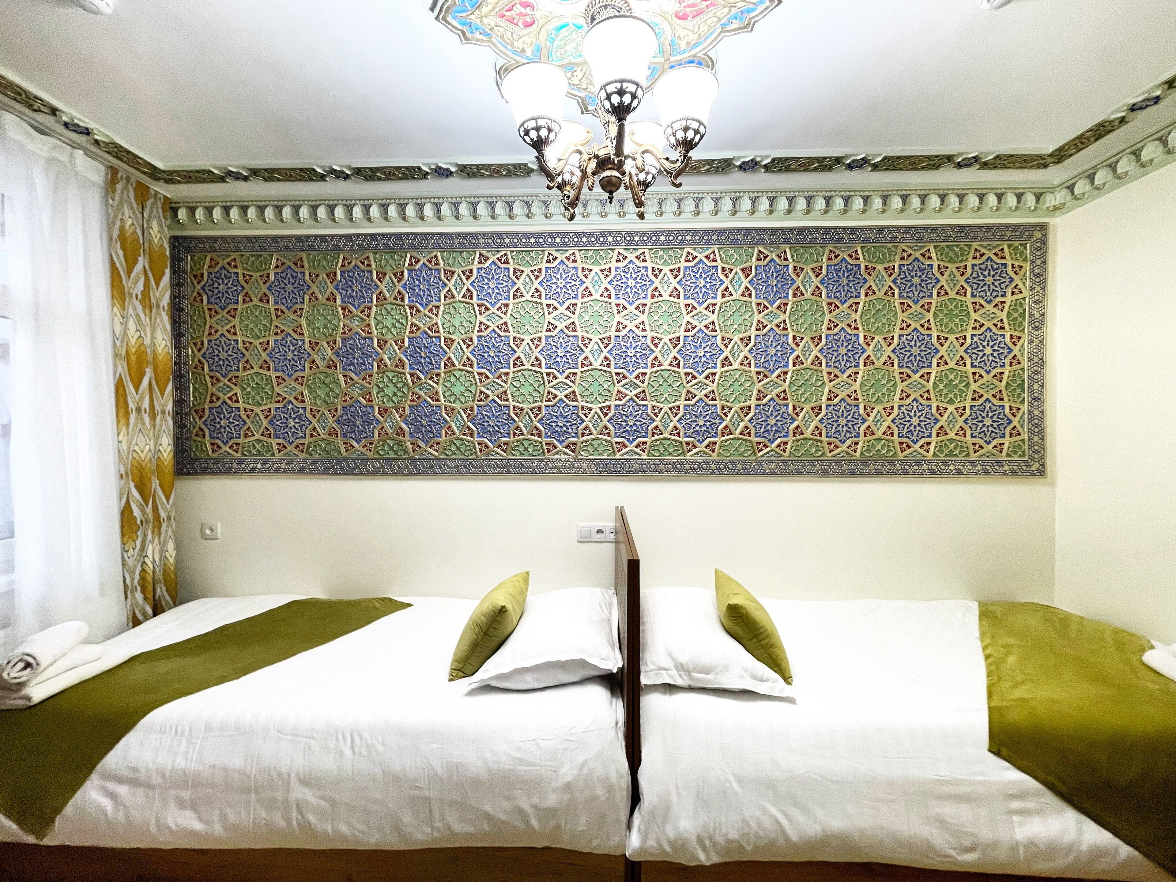 A hotel room with two beds, a chandelier, and a decorative wall with intricate tile work.