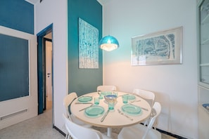 A dining area with a round table set for four, white chairs, a blue pendant light, and two framed artworks on the walls.