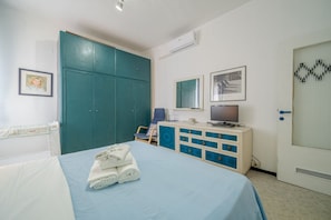 A bedroom with a bed, a desk with a computer, a TV, and a wardrobe.