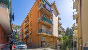 A multi-story residential building with balconies, a narrow street, and parked cars. - GuestHost - Cozy apartment is located in a strategic position to visit the renowned Ligurian Riviera, suitable for families or groups of friends. Convenient for visiting the nearby towns of the Gulf of Tigullio, such as Chiavari, Santa Margherita and Por (Lavagna)