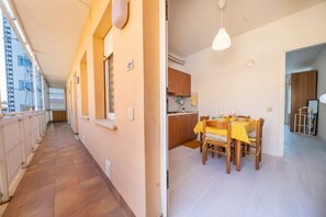 A corridor with a tiled floor, a dining area with a table and chairs, and a kitchen with wooden cabinets.