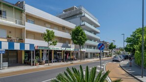 Un edificio de varios pisos con balcones, una pasarela peatonal y locales comerciales.