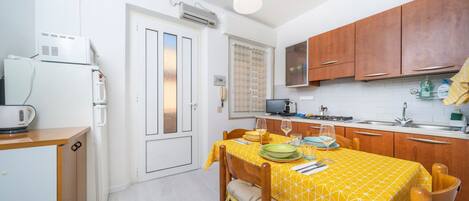 A compact kitchen with a dining table set for two, a refrigerator, a microwave, and wooden cabinets.