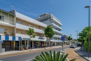 Un edificio de varios pisos con balcones, una pasarela peatonal y locales comerciales.