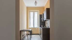 A compact kitchen with a dining area, a window with curtains, and a hanging light fixture.