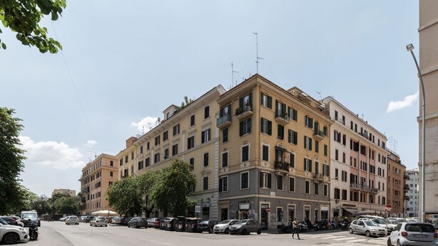 A multi-story building with a corner entrance, parked cars, and a pedestrian crossing.