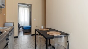 A compact hotel room with a kitchenette, a dining table with two chairs, a bed, and a bathroom visible through a doorway.