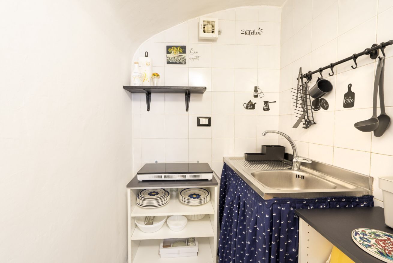 A compact kitchen with white tiles, a stove, a sink, and a hanging rack with utensils.