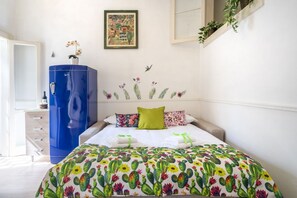 A bedroom with a bed, a blue wardrobe, a wall-mounted shelf with plants, and a framed artwork.