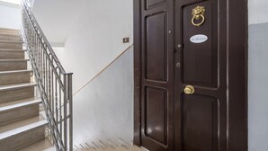 Una escalera conduce a una puerta de madera oscura con un llamador de bronce y un letrero que dice 'La Bombaeta'.