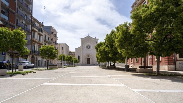 Una calle que lleva a una iglesia con una torre del reloj, rodeada de edificios de varios pisos y árboles.